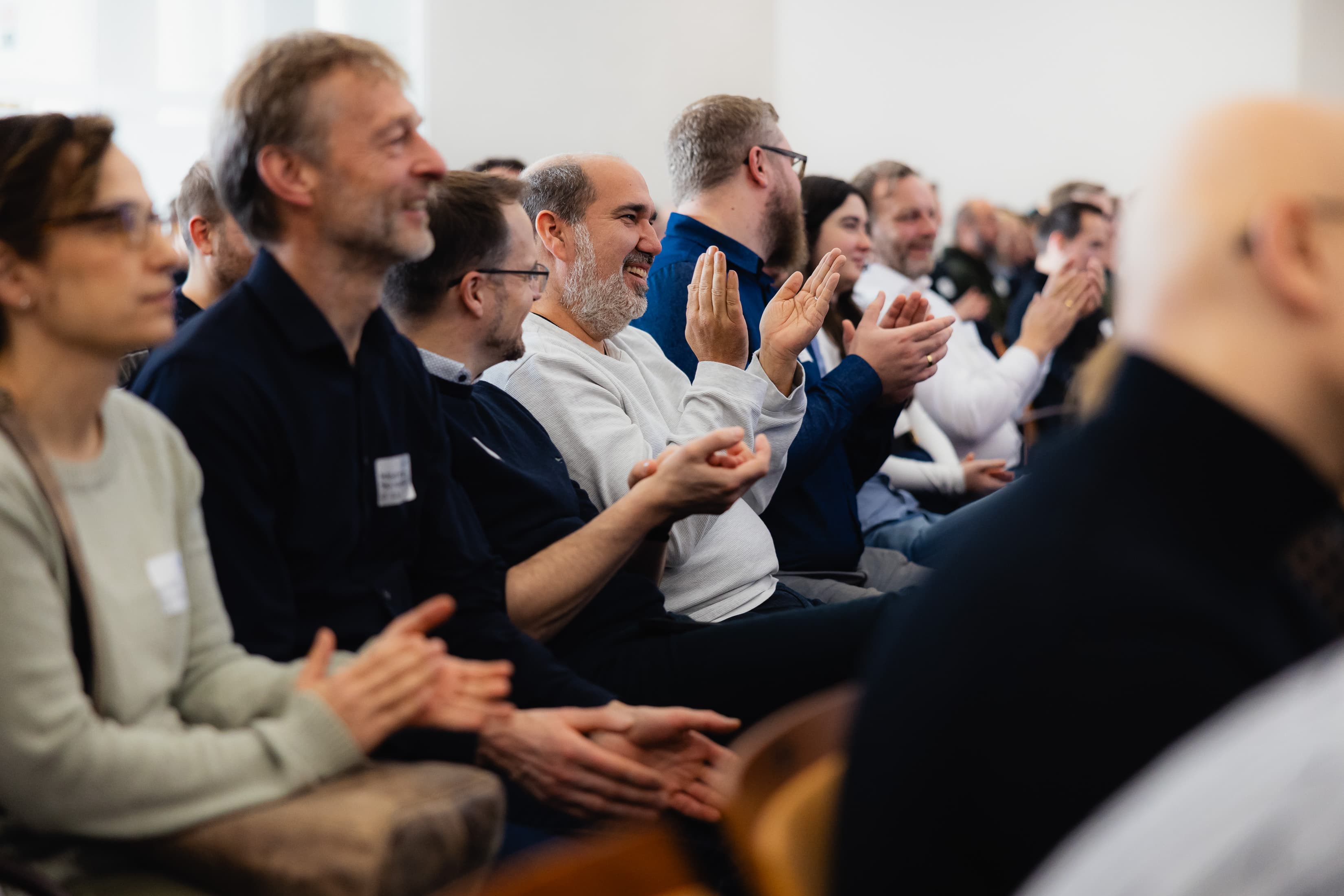 Mitarbeitende aus der IT der WERTGARANTIE Group sitzen nebeneinander, schauen nach vorne und klatschen.