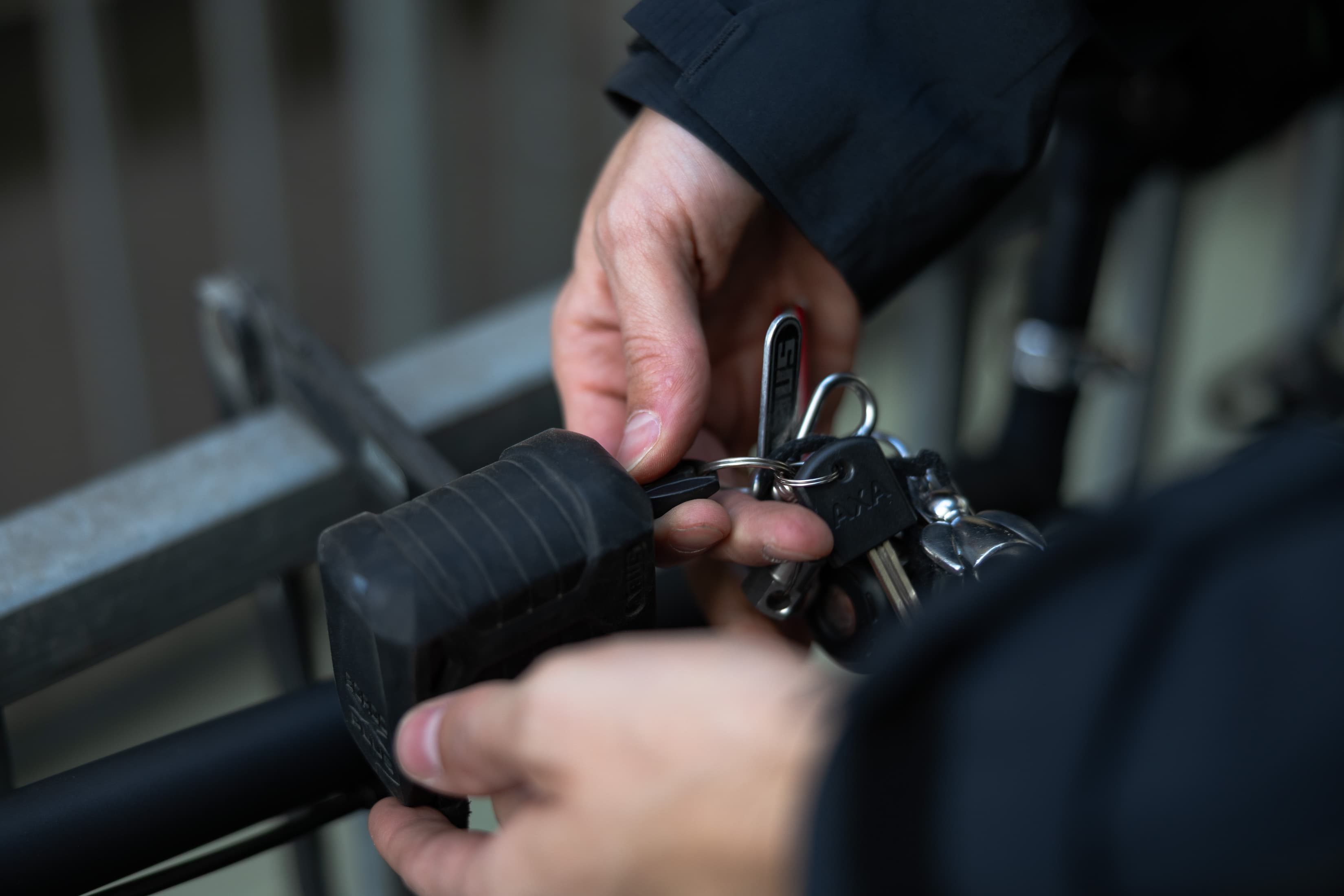 Detailansicht wie zwei Hände ein Fahrradschloss mit einem Schlüssel abschließen.