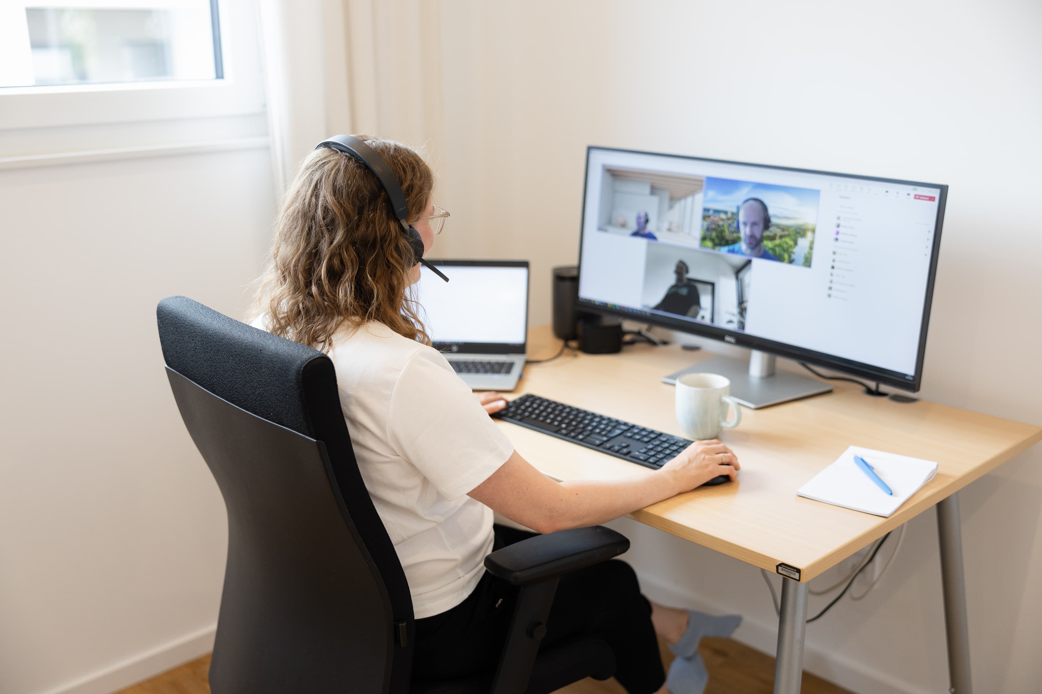 Eine Frau ist von hinten zu sehen, wie sie vor einem Bildschirm sitzt und telefoniert